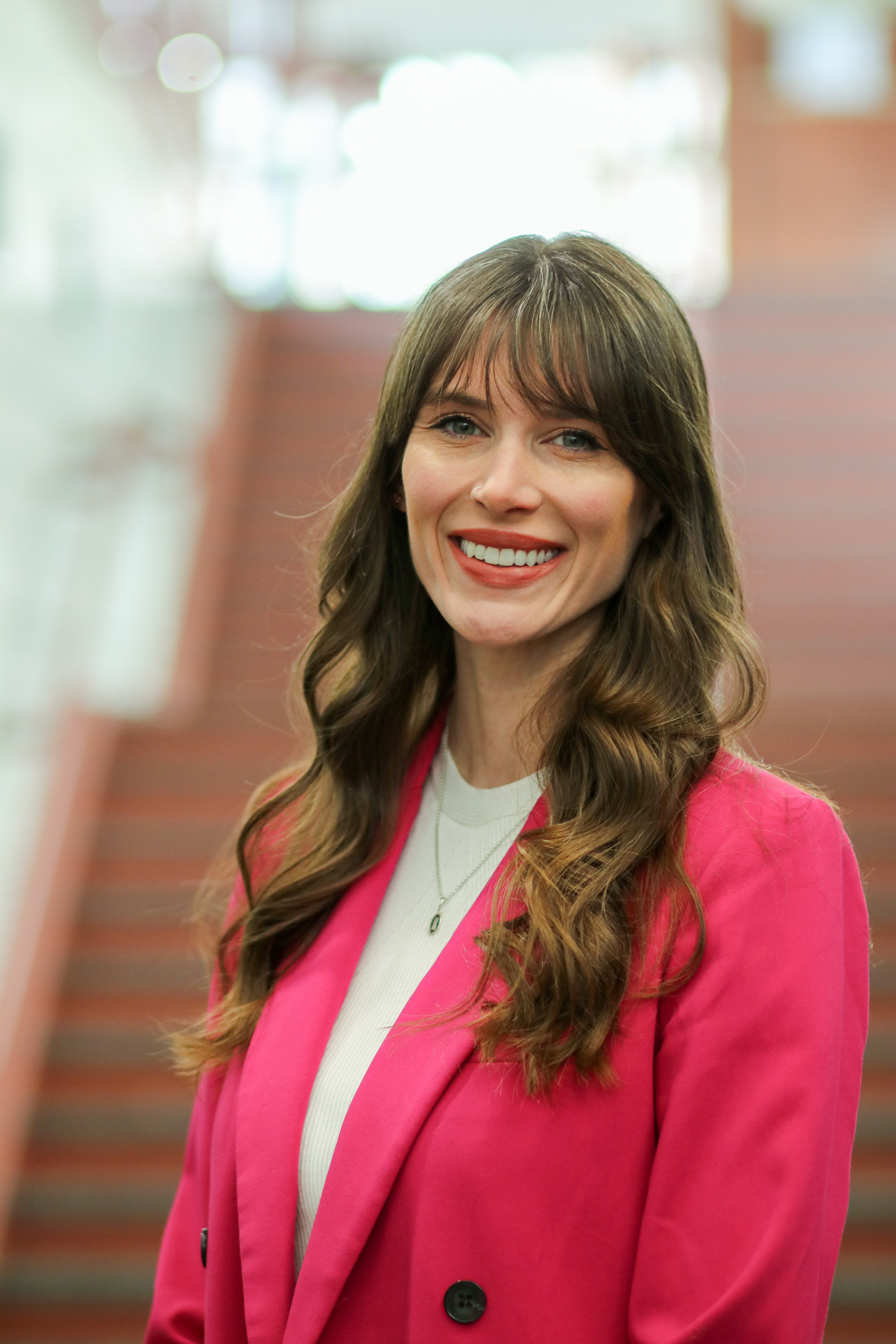 Hanna Lewis, a white woman with dark brown hair, wearing a white shirt with a hot pink jacket