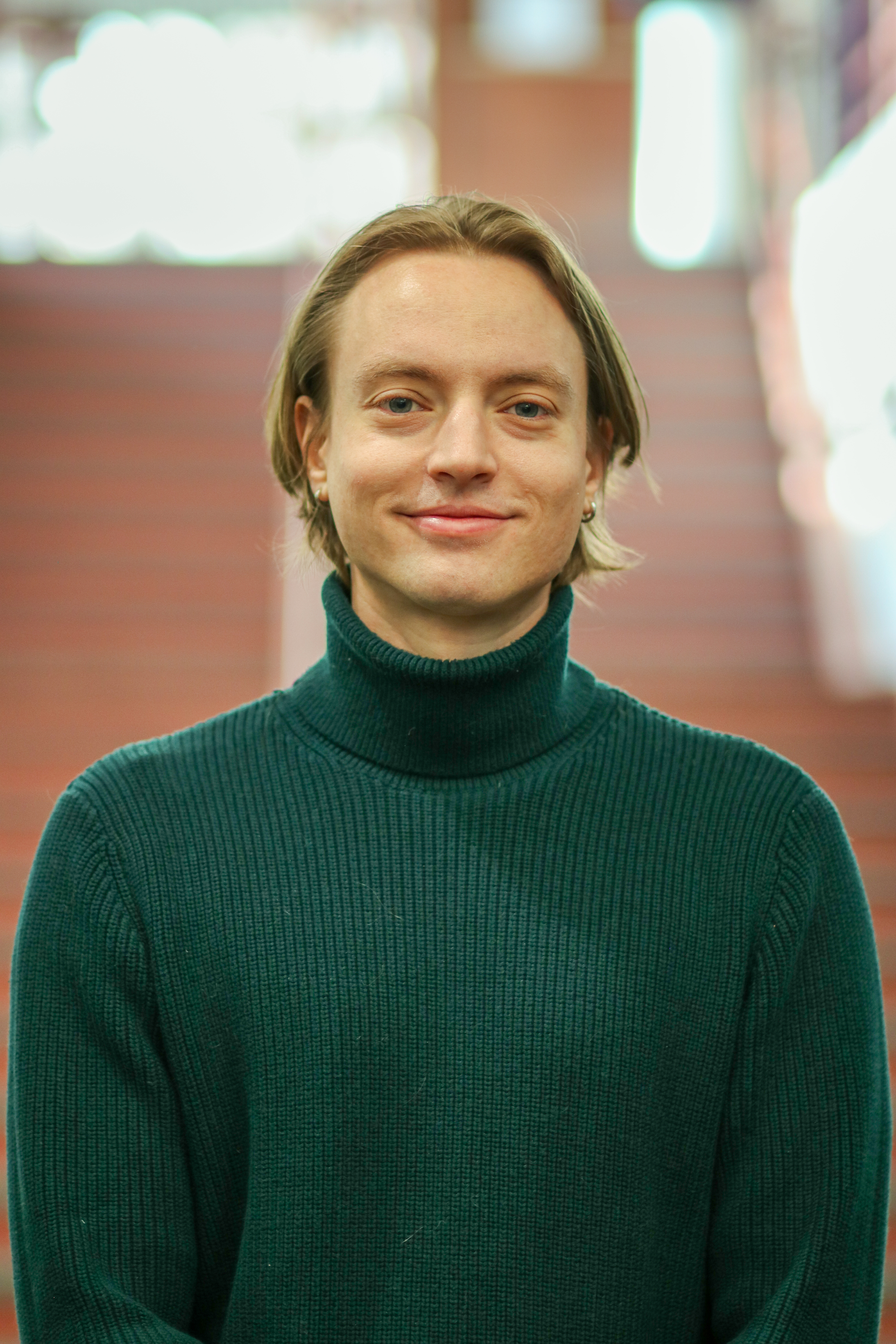 Sasha, who has fair skin and brown hair, wears a dark green turtleneck sweater